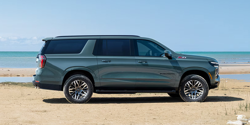 Greenish-gray Chevrolet Suburban Z71 SUV parked on a sandy beach shore.